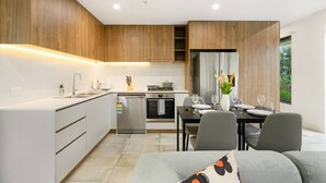 Une cuisine moderne avec des meubles blancs, un coin repas avec une table dressée pour deux personnes, et une vue sur la verdure à l’extérieur.