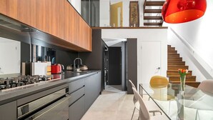 A modern kitchen with a gas stove, a red kettle, and a dining area with a glass table and chairs. - Leichhardt 3-Level Family House | Near CBD (Leichhardt)
