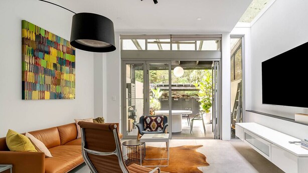 A modern living room with a leather sofa, a unique chair, a large TV, and a colorful abstract painting. - Leichhardt 3-Level Family House | Near CBD (Leichhardt)