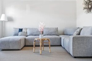 A modern living room with a grey sectional sofa, a small wooden stool with a vase, and a white lamp.