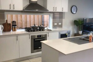 A modern kitchen with white cabinets, a stove, oven, microwave, and a clock on the wall.