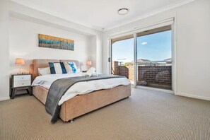 A bedroom with a bed, nightstands, a painting, and a sliding glass door to a balcony.