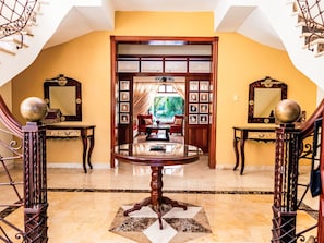 A grand foyer with a marble floor, a central round table, and two side tables with decorative bases.