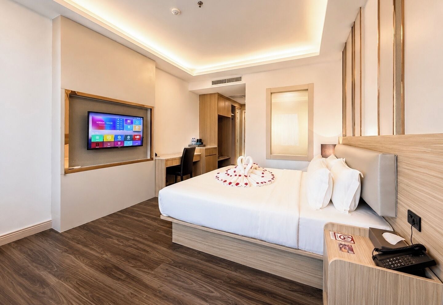 Habitación de hotel con cama, escritorio, silla, televisor montado en la pared y teléfono en la mesita de noche.