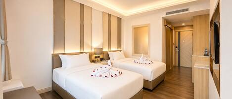 A hotel room with two beds, a flat-screen TV, a desk, and a wooden floor.