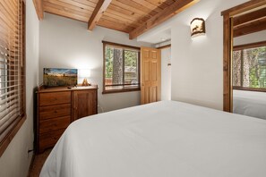 Ein Schlafzimmer mit einem hölzernen Schminktisch, einem Bett, einem Fenster mit Jalousien und einer Wandleuchte.