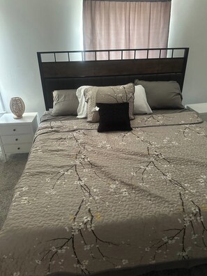 Ein Bett mit einer strukturmuster-Bettdecke mit Zweigdesign, umrahmt von Kissen und einem Zierkissen auf einem Nachttisch.