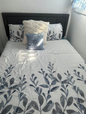 Ein Bett mit dunklem Kopfteil, weißer Bettwäsche und Zierkissen.