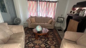 En stue med en beige sofa, et sofabord med et verdenskort, et mønstret tæppe og et vindue med gardiner.
