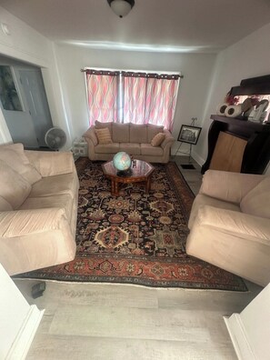 Ein Wohnzimmer mit einem beigen Sofa, einem Couchtisch mit Globus, einem gemusterten Teppich und einem Fenster mit Vorhängen.
