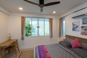 Un dormitorio con cama, escritorio, silla, ventilador de techo y ventana con cortinas.