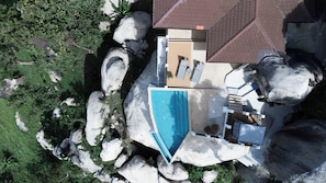 An aerial view of a house with a swimming pool, large rocks, and a garden.