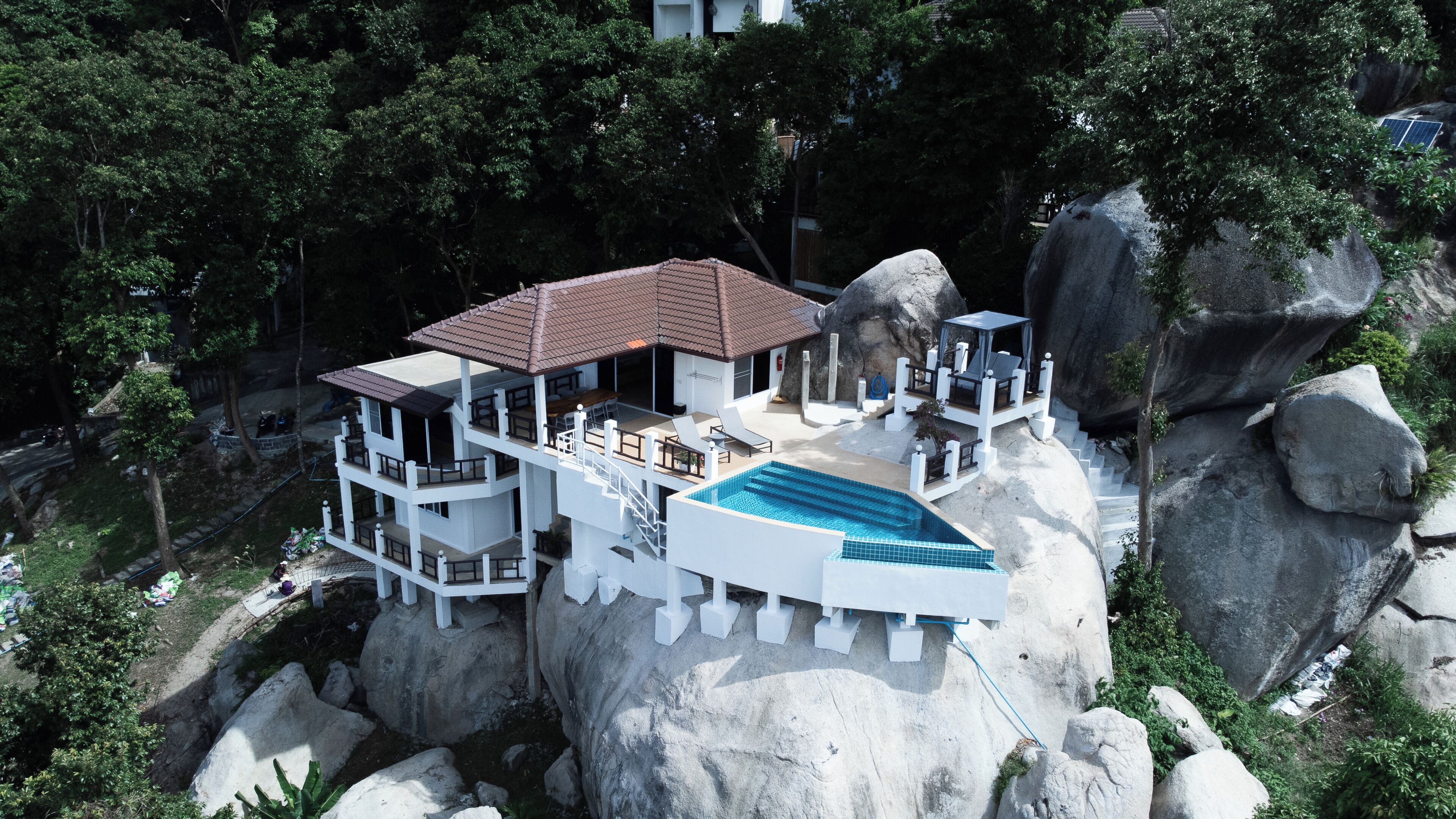 Un complejo turístico de varios niveles con piscina, construido sobre un acantilado rocoso rodeado de árboles.