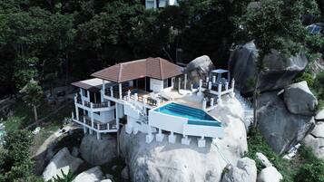 Un complejo turístico de varios niveles con piscina, construido sobre un acantilado rocoso rodeado de árboles.