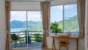 Habitación con balc ón, un escritorio de madera, una silla y vistas a un paisaje montañoso.