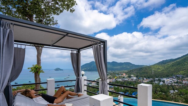Una persona recostada en una cama con vista a una piscina y un paisaje montañoso.