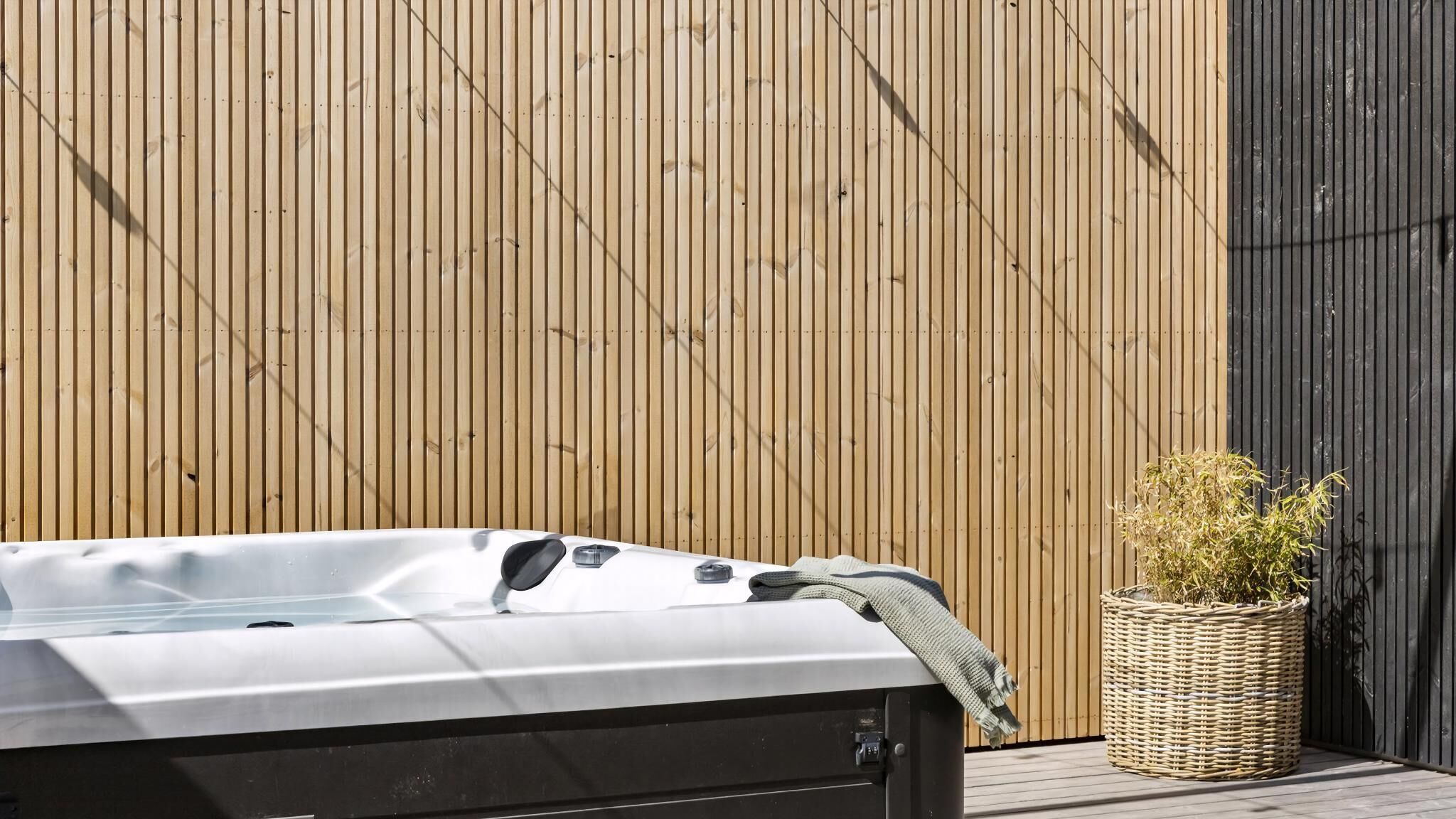 A hot tub on a wooden deck with a bamboo fence in the background.