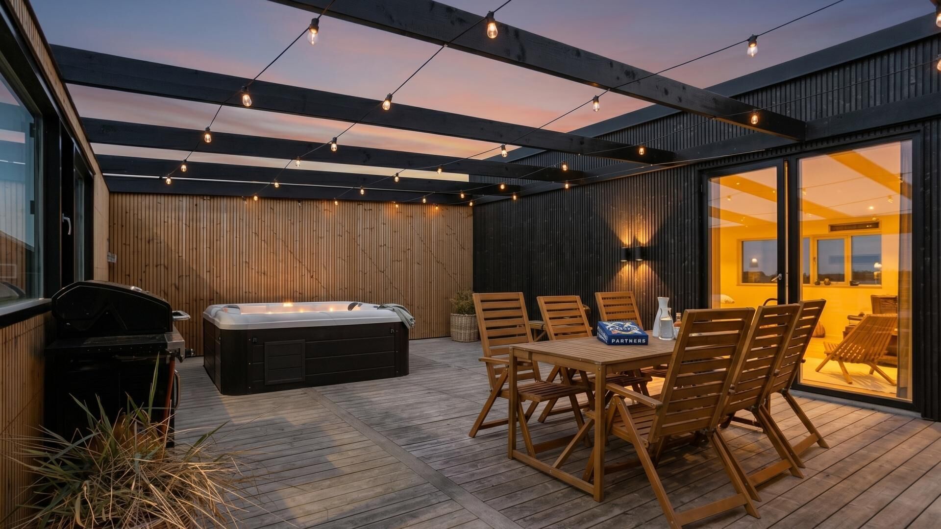 Um pátio externo com banheira de hidromassagem, deck de madeira e uma mesa com cadeiras.