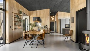 A modern kitchen with a central island, a dining area with a wooden table and leather chairs, and a built-in fireplace. - VillaVilla 965 - Nr. Lyngby ved Løkken, nordjyllan (Løkken)