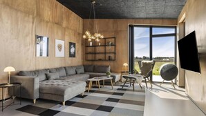 A modern living room with a sofa, armchairs, a coffee table, a chandelier, a TV, and a large window offering a view. - VillaVilla 965 - Nr. Lyngby ved Løkken, nordjyllan (Løkken)