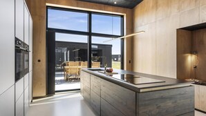 A modern kitchen with a large island, wooden cabinetry, and a view of the outdoors. - VillaVilla 965 - Nr. Lyngby ved Løkken, nordjyllan (Løkken)