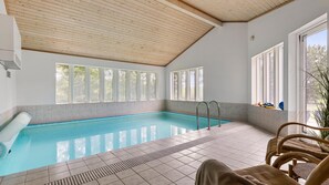 Ein Swimmingpool mit klarem, blauem Wasser, umgeben von gefliesten Böden und großen Fenstern mit Blick auf Grünflächen.