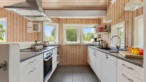 Eine Küche mit Holzwänden, einem Herd, einer Spüle und einem Fenster mit Blick auf Grünflächen.