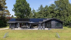 Ett modernt hus med ett solpanelbeklätt tak, en täckt uteplats med utemöbler och en stor gräsmatta.