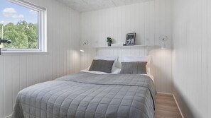 A bedroom with a bed, a window, a shelf with items, and a wall-mounted light. - VillaVilla 960 - Østersøbadet, Lolland/Falster/Møn (Rødby)