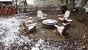 Ett utomhusområde med sittplatser, täckt av snö, med en eldstad och trästolar.