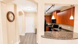 A hallway leading to a kitchen with wooden cabinets, granite countertops, and pendant lighting. - Sleepover | Lavish 1BD/1BA + Pool - Little Rock (North Little Rock)