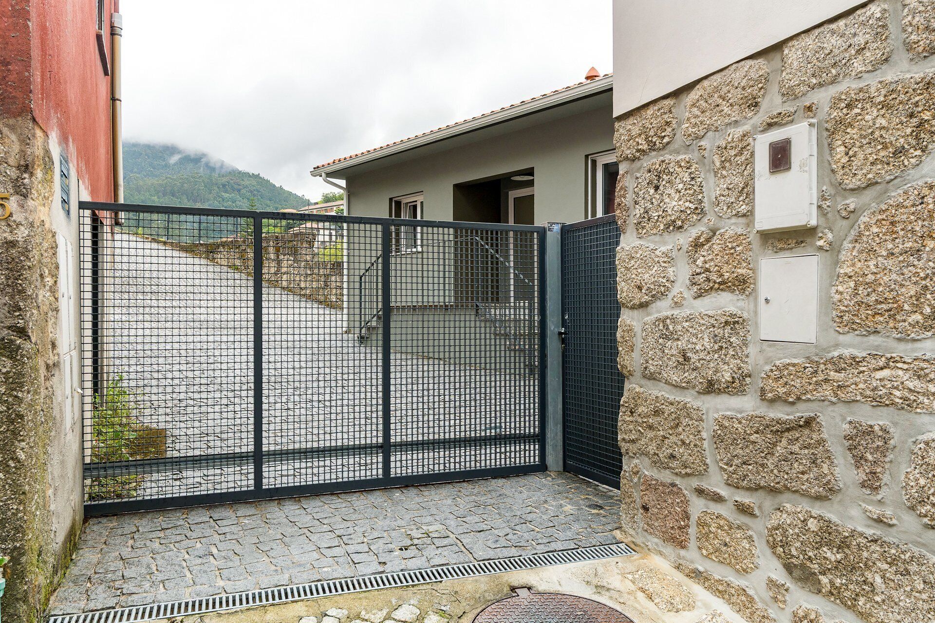 Un mur de pedra, una reixa metàl·lica i un pati pavimentat.