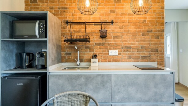 Eine moderne Küche mit Backsteinwand, zwei Pendelleuchten, einer Mikrowelle, einer Kaffeemaschine und einem kleinen Kühlschrank.