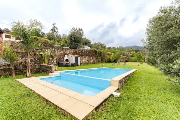 A rectangular swimming pool with a stone edge, surrounded by a grassy lawn and a stone wall. - Charming Retreat with Pool (Amares)
