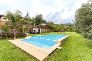 Une piscine rectangulaire bordée de pierres, entourée d’une pelouse et d’un mur en pierre.