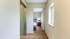 Ein schmaler Flur mit Holzboden, einem Bett mit gemusterten Textilien und einer Kommode mit Schubladen.