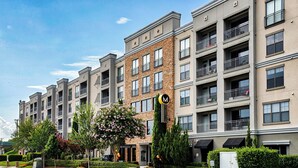 A multi-story residential building with balconies, a central entrance, and a landscaped front yard.
