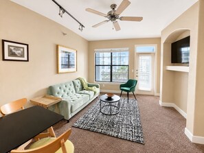 A living room with a sofa, chairs, a coffee table, a ceiling fan, and a TV.
