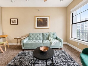 A living room with a light green sofa, a black coffee table, a patterned rug, and a window with a view of buildings.