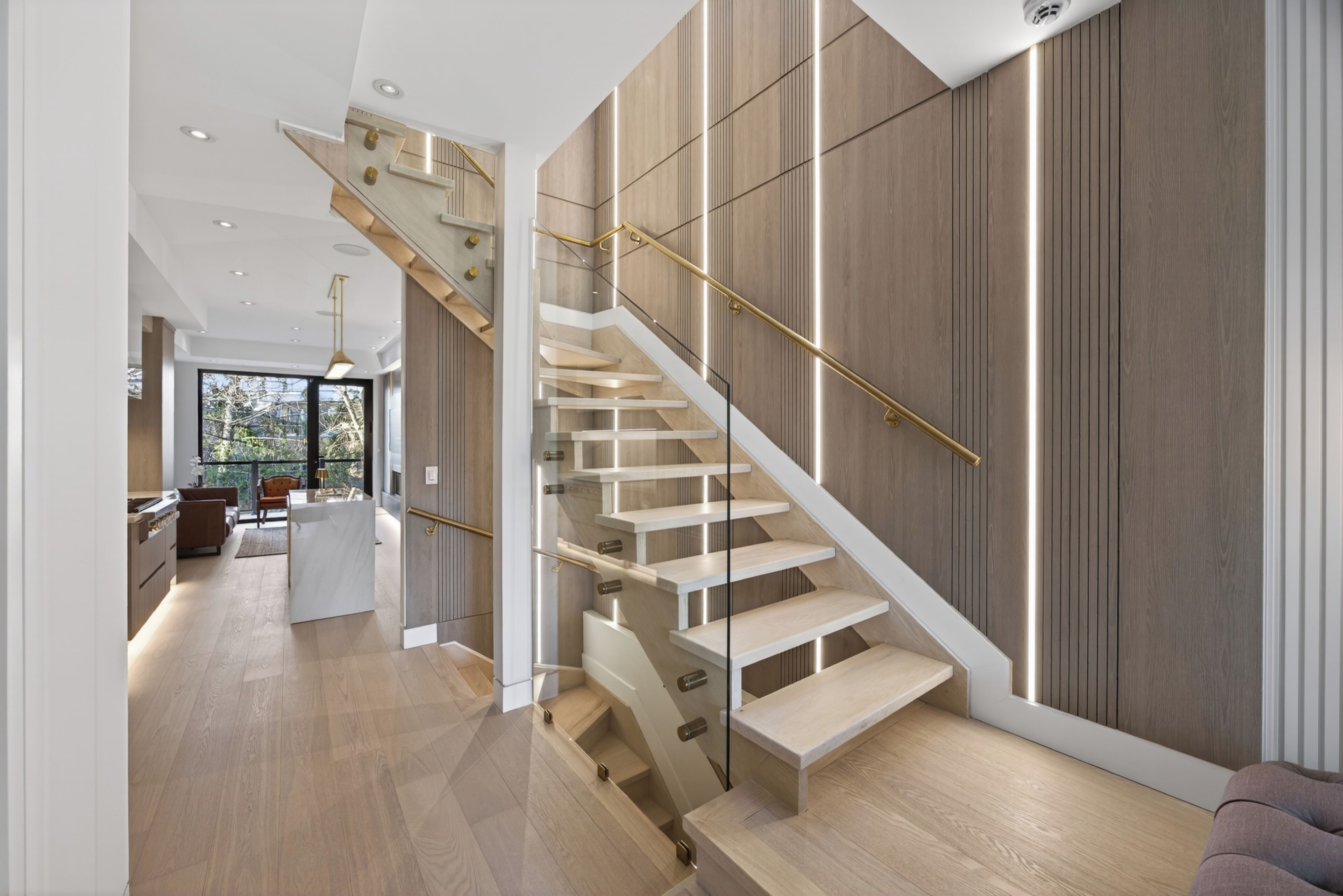 Un interior modern amb una escala, terres de fusta i una zona de cuina.