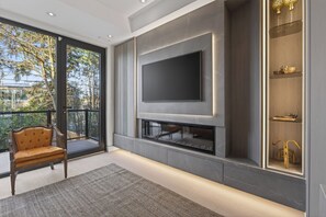 Un salon moderne doté d’un grand téléviseur, d’une cheminée et de portes vitrées donnant sur un balcon.