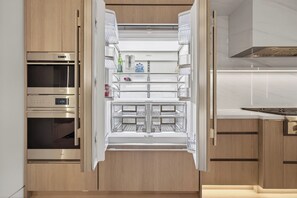 Une cuisine moderne dotée d’un four encastré, d’un réfrigérateur à plusieurs étagères et de meubles de rangement en bois.
