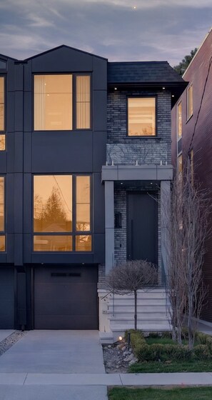 Une maison moderne à deux étages, dotée de grandes fenêtres, d’un garage et d’un jardin bien entretenu.