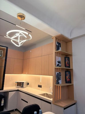 A modern kitchen with a built-in microwave, a sink, and a wooden shelf with artwork. - couple cozy apartment (Ghaziabad)