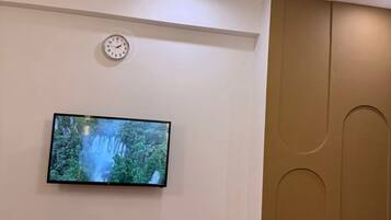 A modern living room with a flat-screen TV mounted on the wall, a wooden bench, a wall clock, and a unique ceiling light fixture.