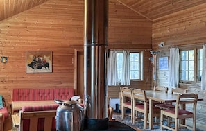 Interno di una baita in legno con un grande stufa, un tavolo da pranzo con sedie, una panca imbottita e un quadro appeso al muro.