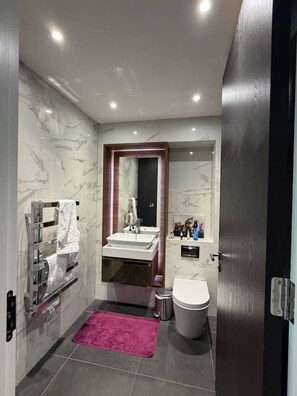Ein modernes Badezimmer mit Marmorwand, einem Doppelwaschbecken, einer Toilette und einer rosa Badmatte.
