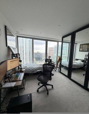 Ein modernes Schlafzimmer mit Schreibtisch, Stuhl und großen Fenstern mit Blick auf die Stadt.