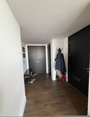 Ein Flur mit Holzboden, einem Kleiderständer mit Jacken, einer Tür und einem Schuhregal mit unterschiedlichen Schuhen.