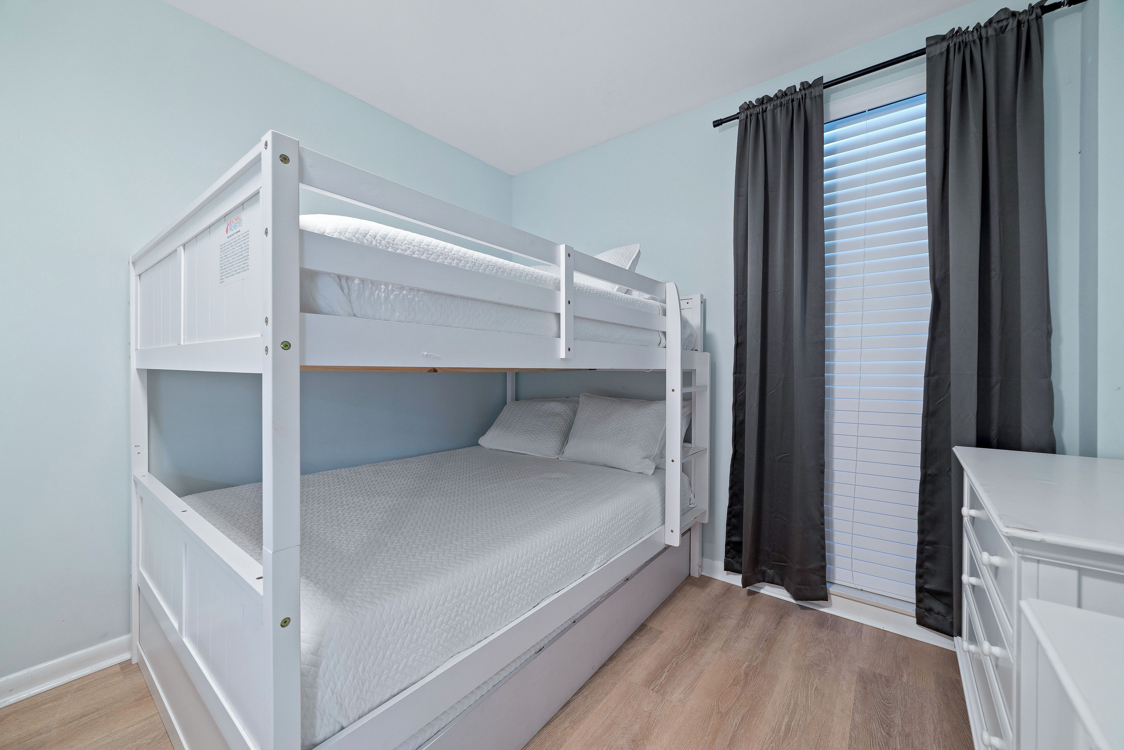 Un lit superposé dans une pièce aux murs bleu clair, avec un plancher en bois et une commode blanche.